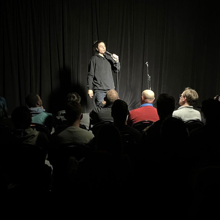 A comedian on stage in front of a full crowd at Club Voltaire